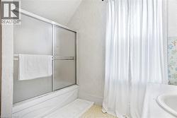 Bathroom featuring a shower-tub combination with sliding frosted glass doors, white vanity with integrated sink, and white textured walls - 