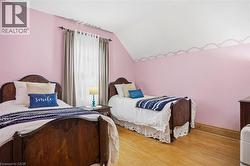 Room featuring light pink walls with a decorative border, wood-finish flooring, and a window with sheer and opaque drapes - 