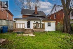 Backyard featuring a wooden deck with railing, direct access from the house, a lower wood staircase, and multiple stone pavers across the lawn - 