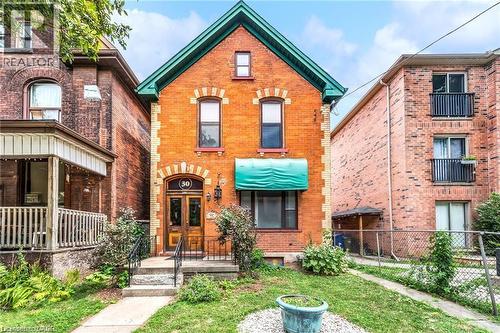Brick facade home featuring a teal gable roof, matching window awning, and a wooden double-door entry - 30 Victoria Avenue N, Hamilton, ON - Outdoor