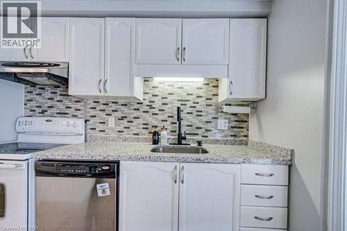 Kitchen featuring white cabinetry with brushed nickel hardware, a multi-tone mosaic tile backsplash, light-colored speckled countertops, a stainless steel sink with a matte black faucet, and a stainle - 854 Elgin Street N, Cambridge, ON 