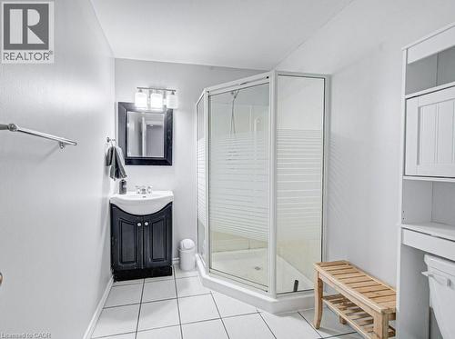 Compact bathroom featuring a corner shower with frosted glass, a vanity with a white basin and dark cabinetry, a framed mirror, and a three-light fixture - 854 Elgin Street N, Cambridge, ON 