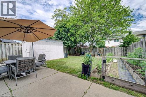 Expansive backyard featuring a concrete patio, grassy lawn, mature trees, wood fence, and raised garden beds - 854 Elgin Street N, Cambridge, ON 