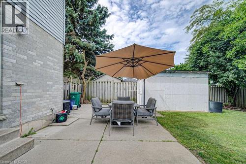 Paved patio area featuring a detached storage shed, privacy fencing, and a perimeter of mature trees - 854 Elgin Street N, Cambridge, ON 