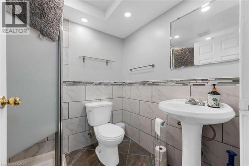 Bathroom featuring a pedestal sink with a single-handle faucet, a toilet, and a tiled accent wall - 338 East 24Th Street, Hamilton, ON 