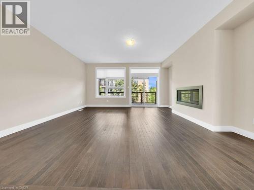 Spacious room with dark wood-finish flooring, light neutral-toned walls, a built-in linear fireplace, and white baseboards - 60 Arkell Road Unit# 51, Guelph, ON 