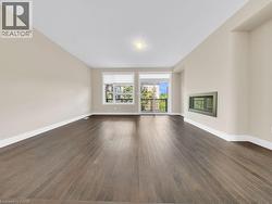 Spacious room with dark wood-finish flooring, light neutral-toned walls, a built-in linear fireplace, and white baseboards - 