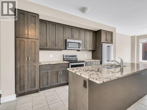 Kitchen featuring wood-finish cabinetry, stainless steel appliances, granite countertops, and light-toned tile flooring - 60 Arkell Road Unit# 51, Guelph, ON 