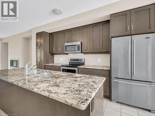 Kitchen featuring a large island with a double basin sink, stainless steel appliances, extensive cabinetry, and light-toned tile flooring - 60 Arkell Road Unit# 51, Guelph, ON 