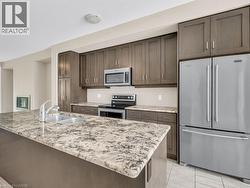 Kitchen featuring a large island with a double basin sink, stainless steel appliances, extensive cabinetry, and light-toned tile flooring - 