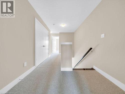 Carpeted hallway featuring neutral wall tones, white trim, recessed lighting, and a dark wood handrail - 60 Arkell Road Unit# 51, Guelph, ON 