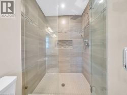 Frameless glass shower enclosure featuring large format wall tiles, a decorative mosaic accent band, a built-in shower niche, and a rainfall showerhead with a handheld spray - 