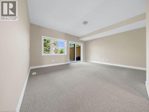 Spacious room featuring neutral carpeting, light beige walls, white trim, a large window, and a sliding glass door - 60 Arkell Road Unit# 51, Guelph, ON 
