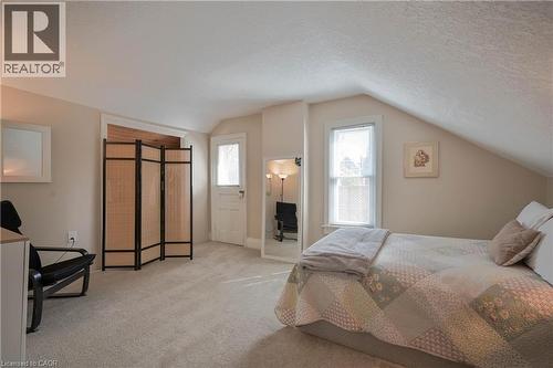 Carpeted room with sloped ceilings, featuring a recessed doorway, a paneled door with glass insert, and a window with white trim - 25 Ahrens Street W, Kitchener, ON - Indoor Photo Showing Bedroom