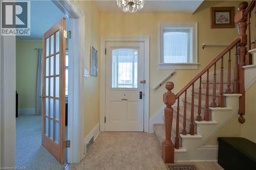 Entrance foyer featuring a light wood French door, staircase with wood banister and carpeted steps, overhead chandelier, and a front entry door with transom window - 25 Ahrens Street W, Kitchener, ON - Indoor Photo Showing Other Room