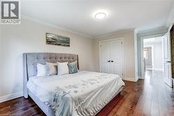 Bedroom featuring wood-finish flooring, white baseboards, crown molding, and a flush-mount ceiling light - 
