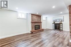 Spacious room featuring wood-finish flooring, a brick fireplace with a wood mantle, recessed lighting, and white baseboards - 