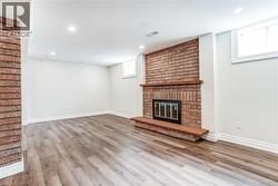 Spacious room featuring a brick fireplace with a wood mantle, wood-finish flooring, recessed lighting, and white baseboards - 