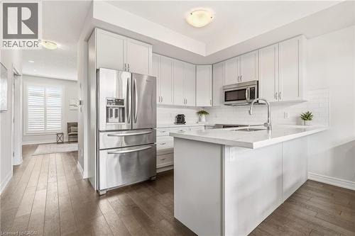 Contemporary kitchen featuring white cabinetry, stainless steel appliances, a subway tile backsplash, a kitchen island with a single basin sink, and wood-finish flooring - 4171 Palermo Common, Burlington, ON - Indoor Photo Showing Kitchen With Stainless Steel Kitchen With Upgraded Kitchen