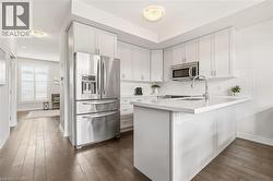 Contemporary kitchen featuring white cabinetry, stainless steel appliances, a subway tile backsplash, a kitchen island with a single basin sink, and wood-finish flooring - 