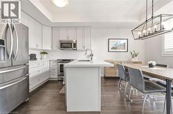 Kitchen featuring white cabinetry, stainless steel appliances, a center island with a sink, white subway tile backsplash, and dark wood-finish flooring - 