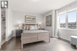 Spacious bedroom featuring dark wood-finish flooring, light-colored walls, and a large window providing natural illumination - 