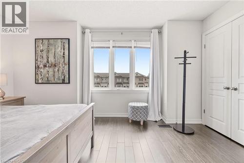 Bright room featuring a large three-panel window, wood-finish flooring, and white baseboards - 4171 Palermo Common, Burlington, ON - Indoor Photo Showing Bedroom
