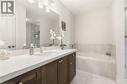 Bathroom featuring a dual-basin vanity with a white countertop and dark wood-finish cabinetry, a large mirror, and an integrated bathtub with tiled surround - 