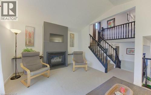 Living space featuring a central fireplace with a matte gray surround, carpeted flooring, and a multi-level staircase with dark wood balusters and handrails - 108 Clearwater Crescent, Waterloo, ON - Indoor With Fireplace