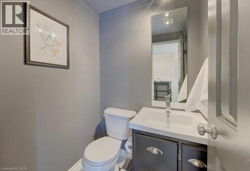 Powder room featuring a pedestal toilet, vanity with integrated white sink, chrome faucet, and dark wood-finish cabinetry with silver-tone hardware - 108 Clearwater Crescent, Waterloo, ON - Indoor Photo Showing Bathroom