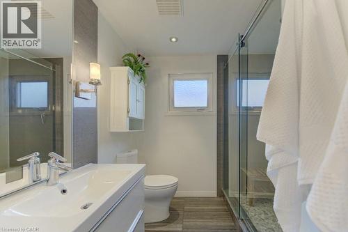 Contemporary bathroom featuring a white vanity with integrated sink, a glass-enclosed shower, wood-finish flooring, a wall-mounted cabinet, and recessed ceiling lighting - 108 Clearwater Crescent, Waterloo, ON - Indoor Photo Showing Bathroom