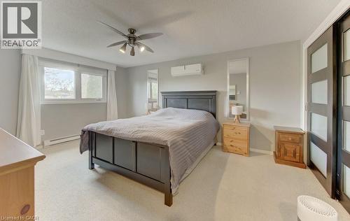 Carpeted interior space featuring light gray walls, white trim, a ceiling fan with integrated lighting, and a wall-mounted climate control unit - 108 Clearwater Crescent, Waterloo, ON - Indoor Photo Showing Bedroom