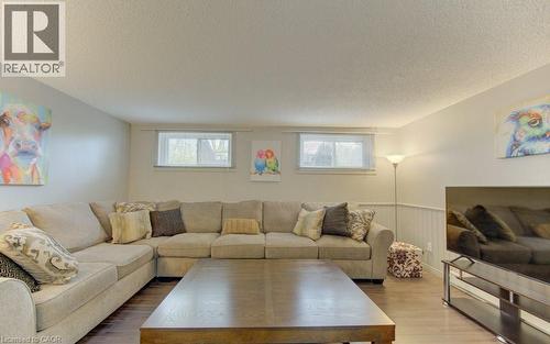 Spacious recreational room featuring wood-finish flooring, two natural light windows, and a built-in white wainscoting accent wall - 108 Clearwater Crescent, Waterloo, ON - Indoor Photo Showing Living Room