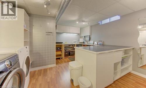 Dedicated laundry area featuring a front-loading washing machine and dryer, ample shelving, tile wall accent, and wood-finish flooring - 108 Clearwater Crescent, Waterloo, ON - Indoor Photo Showing Laundry Room