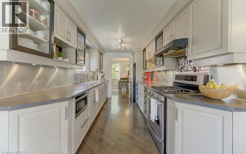 Galley kitchen featuring white paneled cabinetry, dark wood-finish flooring, stainless steel appliances, and a corrugated metal backsplash - 108 Clearwater Crescent, Waterloo, ON - Indoor Photo Showing Kitchen