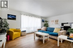 Bright living area featuring wood-finish flooring, white walls, and a large window with white curtains - 
