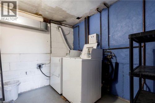 Laundry area featuring white block walls, concrete flooring, exposed utility piping, and a washer and dryer set - 43 Sixth Avenue, Kitchener, ON - Indoor Photo Showing Laundry Room