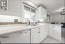 Kitchen featuring dishwasher, a peninsula, light countertops, white cabinetry, and light marble finish floors - 