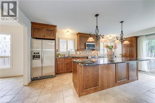 Kitchen featuring a large central island with a dark countertop, wood-finish cabinetry, stainless steel appliances, tile flooring, and two chandelier-style pendant lights - 43 Niska Drive, Waterdown, ON - Indoor Photo Showing Kitchen