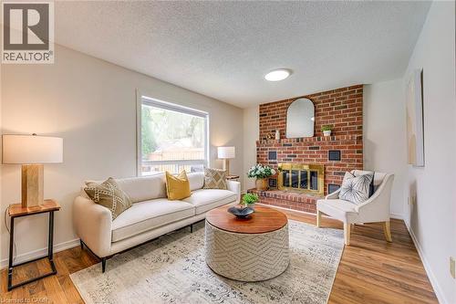 Living area featuring a prominent brick fireplace with a gold-toned insert, wood-finish flooring, a large window, and light-toned walls - 43 Niska Drive, Waterdown, ON - Indoor Photo Showing Living Room With Fireplace