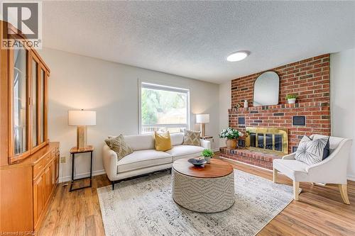 Living space featuring a brick fireplace with a brass firebox, a large window, and wood-finish flooring - 43 Niska Drive, Waterdown, ON - Indoor Photo Showing Living Room With Fireplace