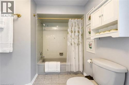Bathroom featuring a built-in bathtub with subway tile surround, neutral-toned floor tile, and a wall-mounted storage cabinet - 43 Niska Drive, Waterdown, ON - Indoor Photo Showing Bathroom