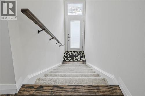 Carpeted staircase featuring a wood-finish handrail with dark metal brackets - 720 Grey Street Unit# 34, Brantford, ON - Indoor Photo Showing Other Room