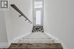 Carpeted staircase featuring a wood-finish handrail with dark metal brackets - 