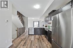 Open-concept kitchen with dark wood-finish cabinetry, stainless steel appliances, white countertops, and wood-finish flooring - 