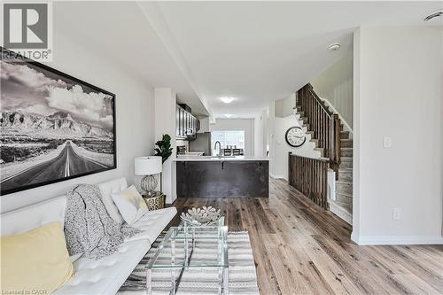 Open-concept living space featuring wood-finish flooring, a kitchen island with a light-toned countertop, dark cabinetry, and a staircase with wood railings - 720 Grey Street Unit# 34, Brantford, ON - Indoor Photo Showing Living Room