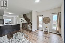 Open-concept living area with wood-finish flooring, white walls, and a staircase featuring dark wood railings - 