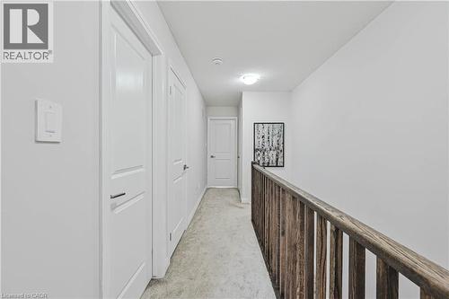 Hallway featuring light gray carpet flooring, white paneled doors, and a natural wood-finish railing - 720 Grey Street Unit# 34, Brantford, ON - Indoor Photo Showing Other Room