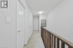 Hallway featuring light gray carpet flooring, white paneled doors, and a natural wood-finish railing - 