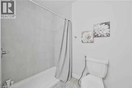 Bathroom featuring a white bathtub, light grey wall tiling, and a white toilet - 720 Grey Street Unit# 34, Brantford, ON - Indoor Photo Showing Bathroom